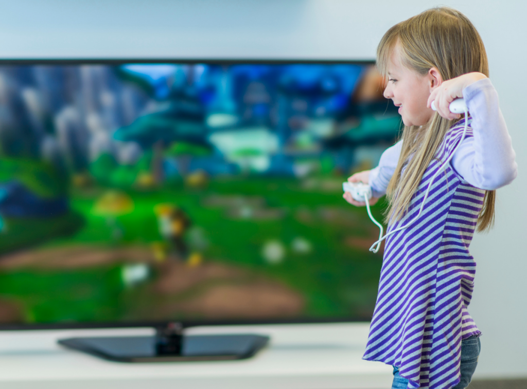 Girl standing in front of a TV holding the controls for a video gaming console